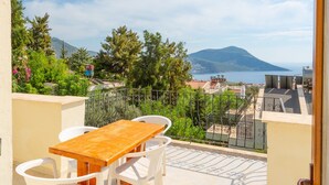 A balcony with a wooden table and white chairs, overlooking a scenic landscape with mountains and a body of water.