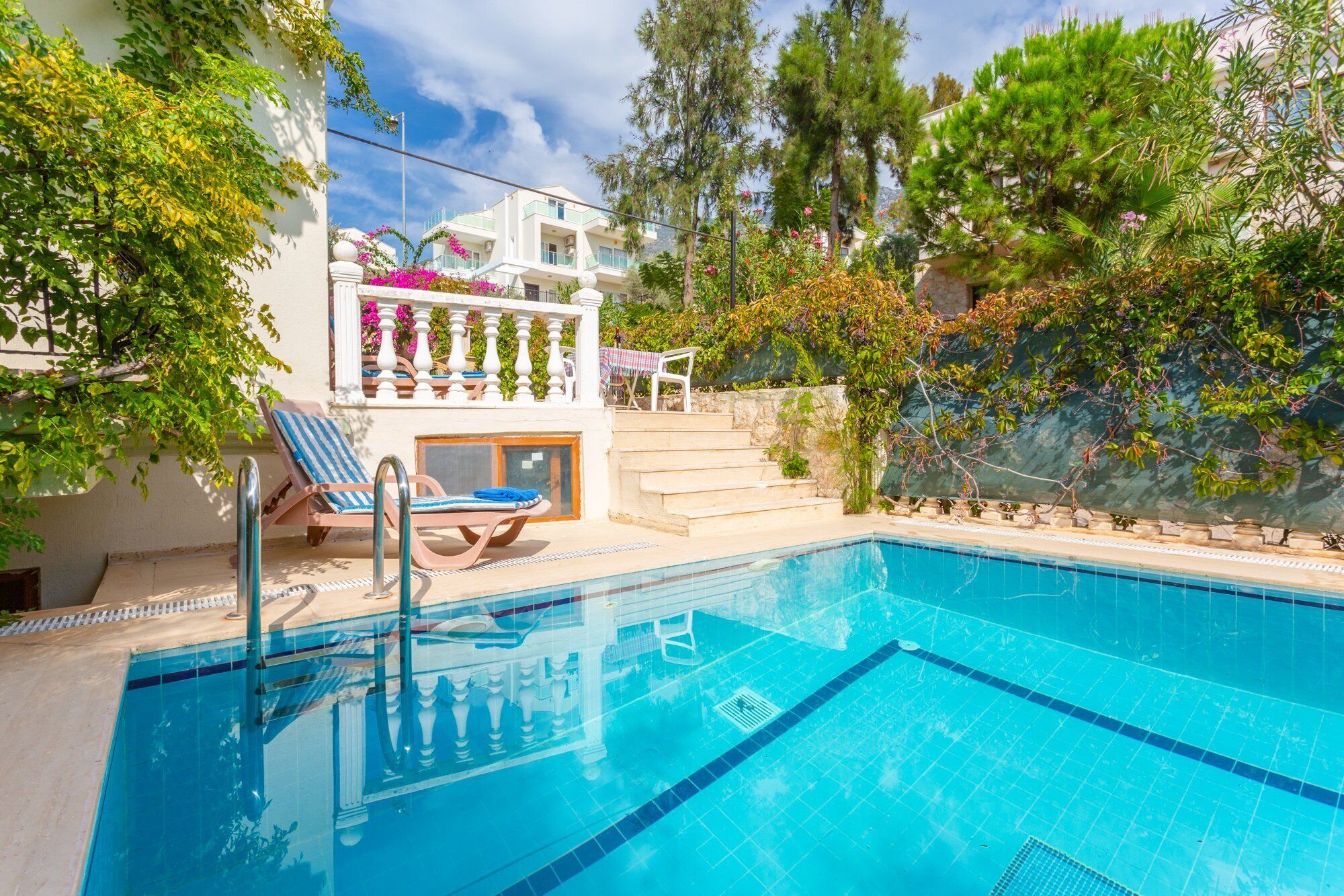 A swimming pool with lounge chairs, a staircase, and a view of a building with balconies.