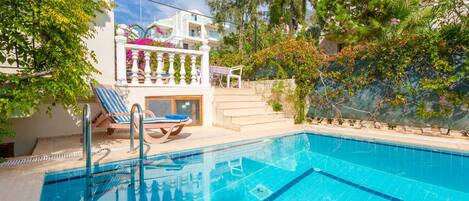 A swimming pool with lounge chairs, a staircase, and a view of a building with balconies.