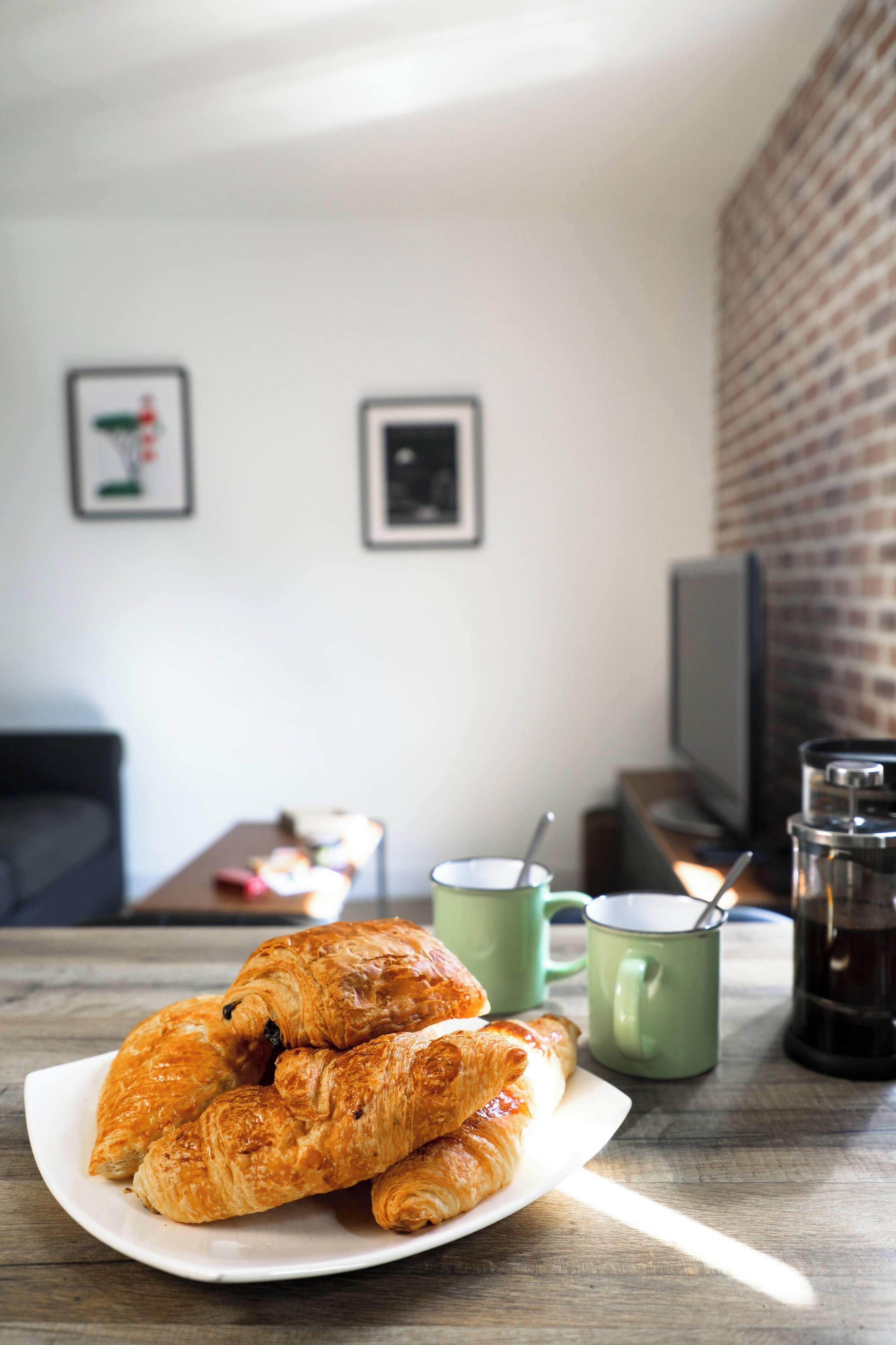 Un plato de croissants sobre una mesa, con dos tazas y una cafetera al fondo.