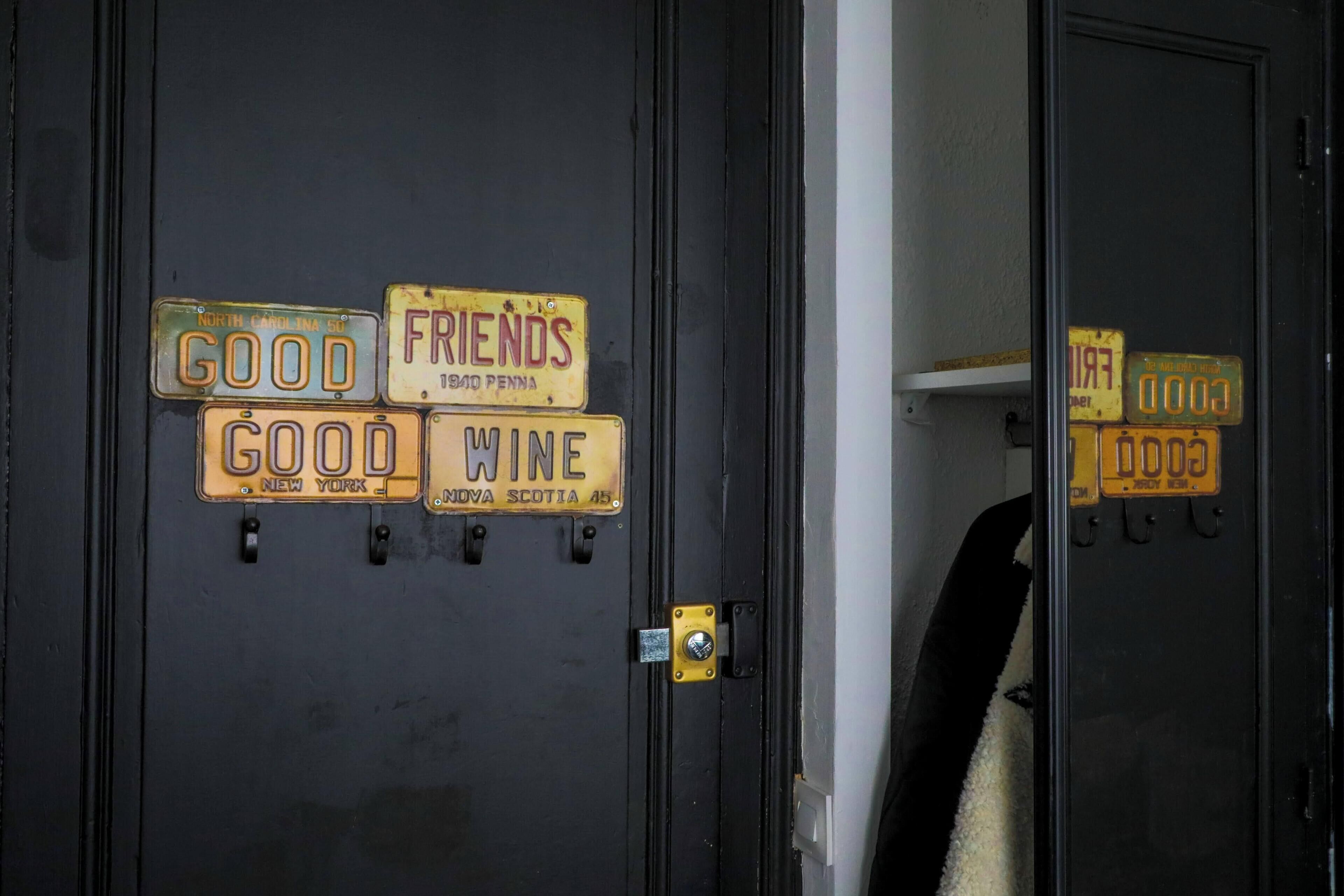 Une porte ornée de plusieurs plaques d’immatriculation, dont les inscriptions sont « GOOD », « FRIENDS » et « WINE ».