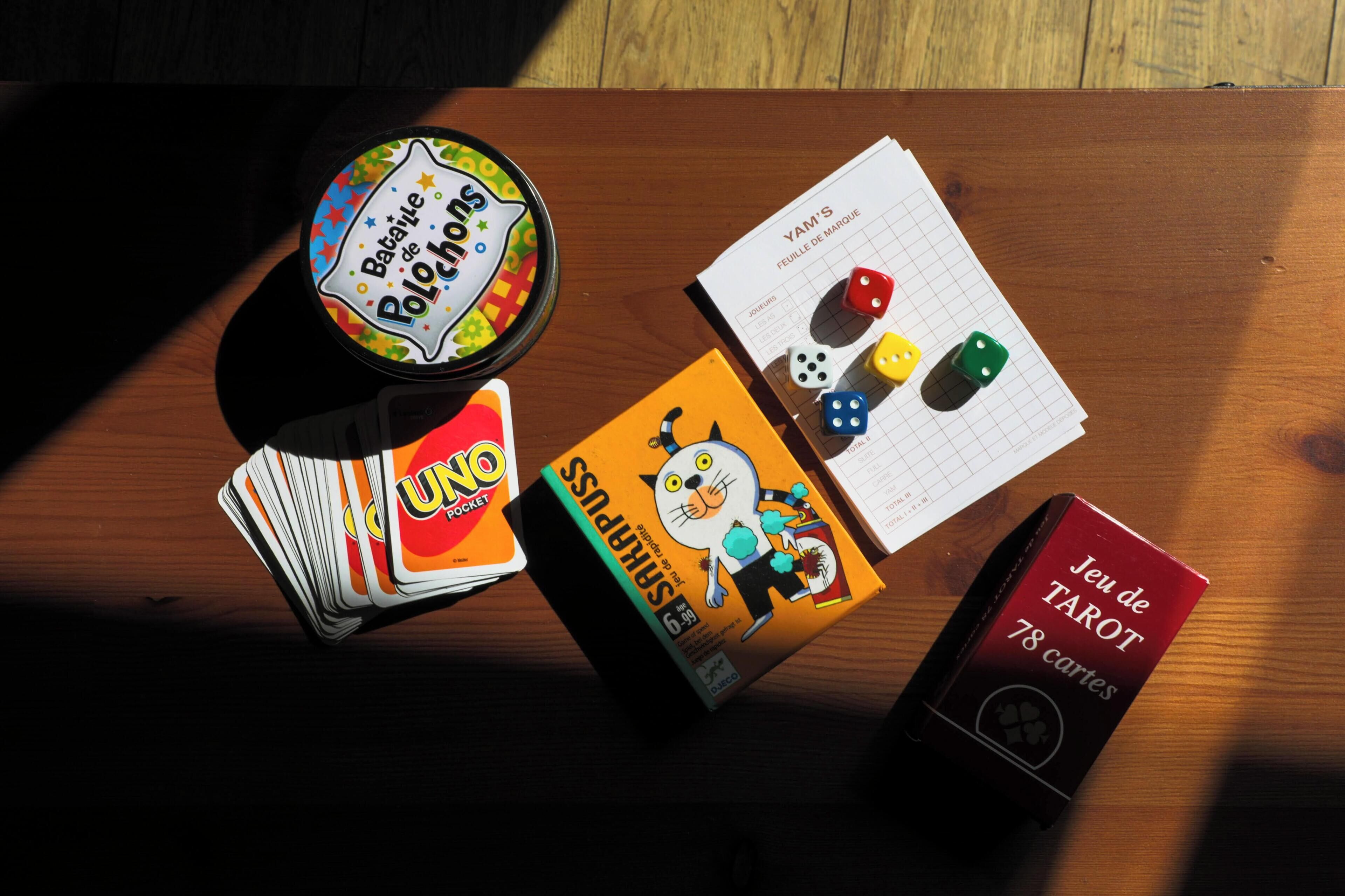 A wooden table with a game box labeled "Bataille de Pochards," a deck of cards, dice, and a tarot card box.