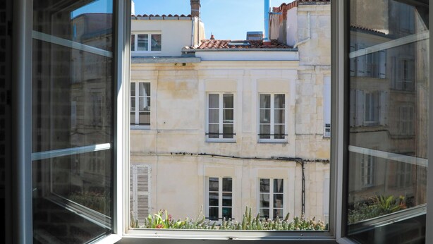 Vista a través de una ventana de un edificio con múltiples ventanales y tejado de tejas.