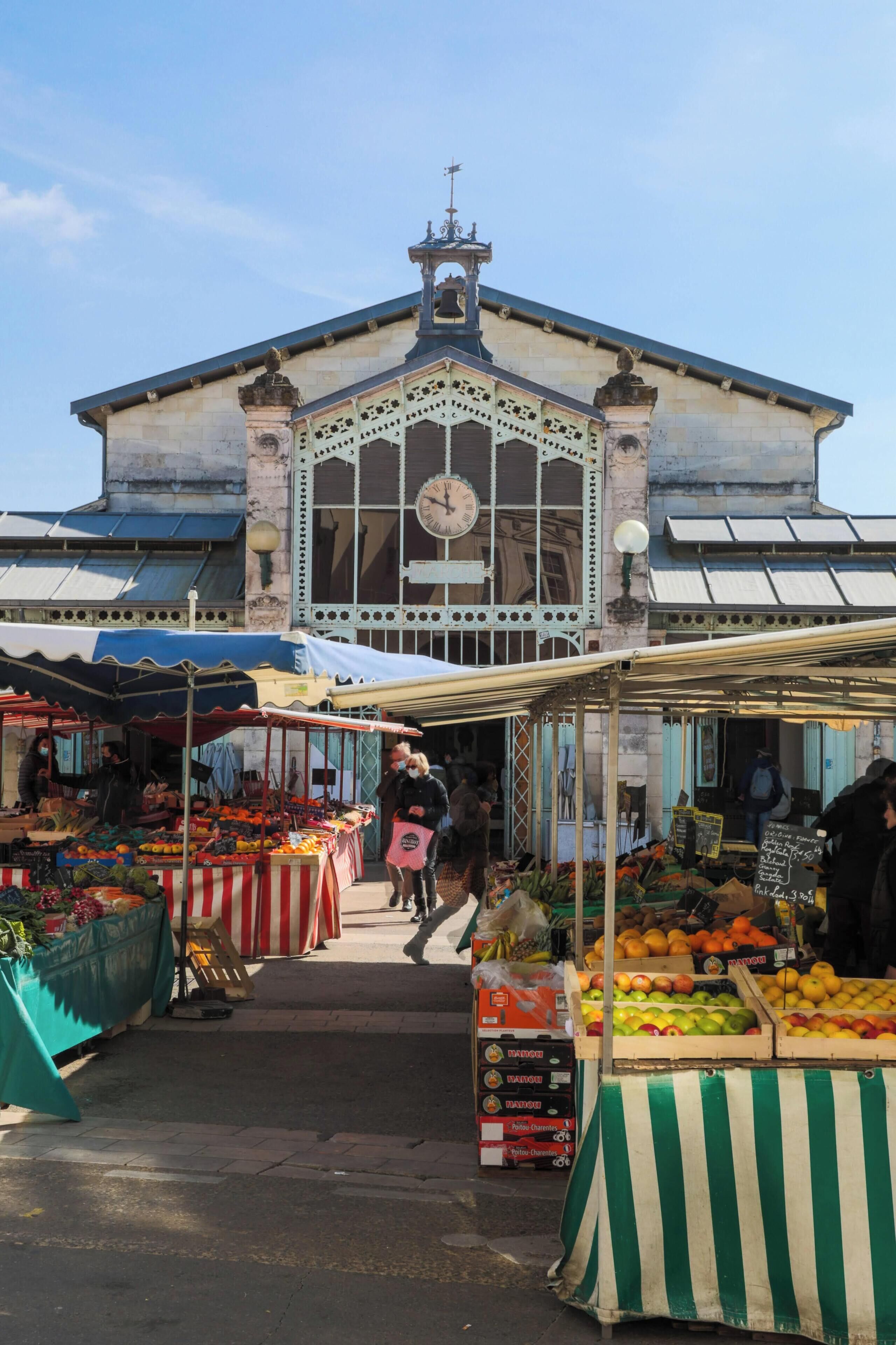 Un marché en plein air avec des étals de fruits et, en arrière-plan, un bâtiment historique.