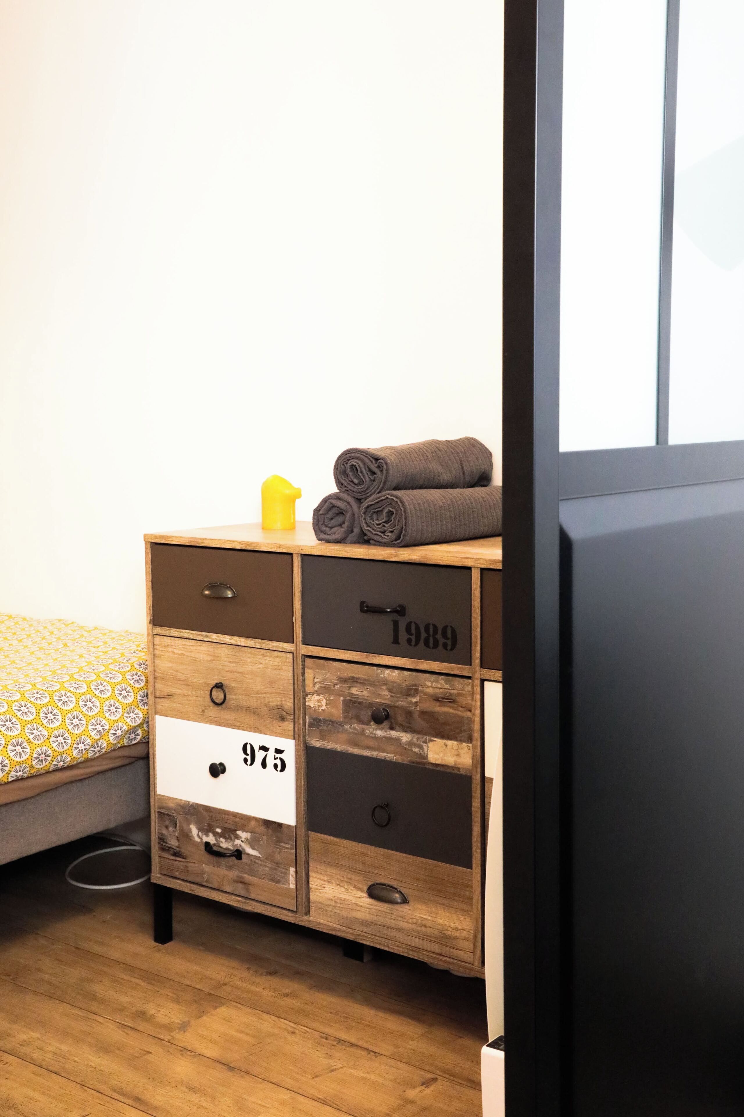 Ein Schlafzimmer mit einem hölzernen Schminktisch, einem Bett mit gemustertem Überwurf und einem Fenster.
