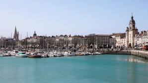 Un puerto deportivo con barcos amarrados, una torre destacada y edificios históricos al fondo.