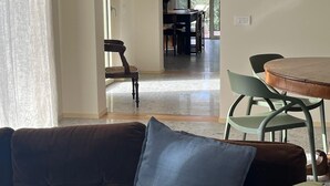 A living room with a brown sofa, a blue pillow, and a green pillow. There is a dining area with a table and chairs in the background. - Elegant apartment, villa surrounded by greenery a stone's throw from the lake and the village (Garda)