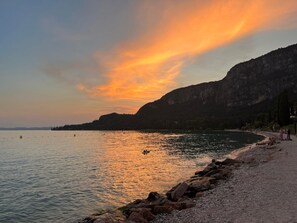 A coastal scene with a rocky shoreline, calm water, and a sunset.