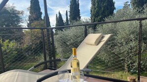 A sunlit outdoor seating area with a table, a bottle of wine, and a glass. - Elegant apartment, villa surrounded by greenery a stone's throw from the lake and the village (Garda)