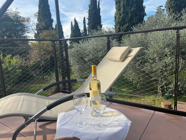 A sunlit outdoor seating area with a table, a bottle of wine, and a glass.
