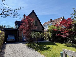 Traditional home surrounded by lush greenery, featuring a steeply pitched roof and brick exterior.