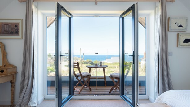 A room with a large sliding glass door leading to an outdoor area with a table and chairs, a wooden bench, and a view of the sea. - Family Beach House - Direct Access to Sennen Cove  Perfect for Summer Holidays (Sennen Cove)