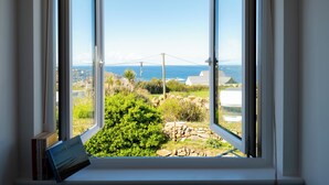 A window with a view of the sea and a coastal landscape, including a stone wall and greenery. - Family Beach House - Direct Access to Sennen Cove  Perfect for Summer Holidays (Sennen Cove)