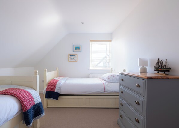A bedroom with two beds, a dresser, a window with blinds, and a ship model on the dresser. - Family Beach House - Direct Access to Sennen Cove Perfect for Summer Holidays (Sennen Cove)