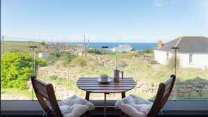 A room with a table and two chairs facing a scenic view of the sea and countryside. - Family Beach House - Direct Access to Sennen Cove  Perfect for Summer Holidays (Sennen Cove)