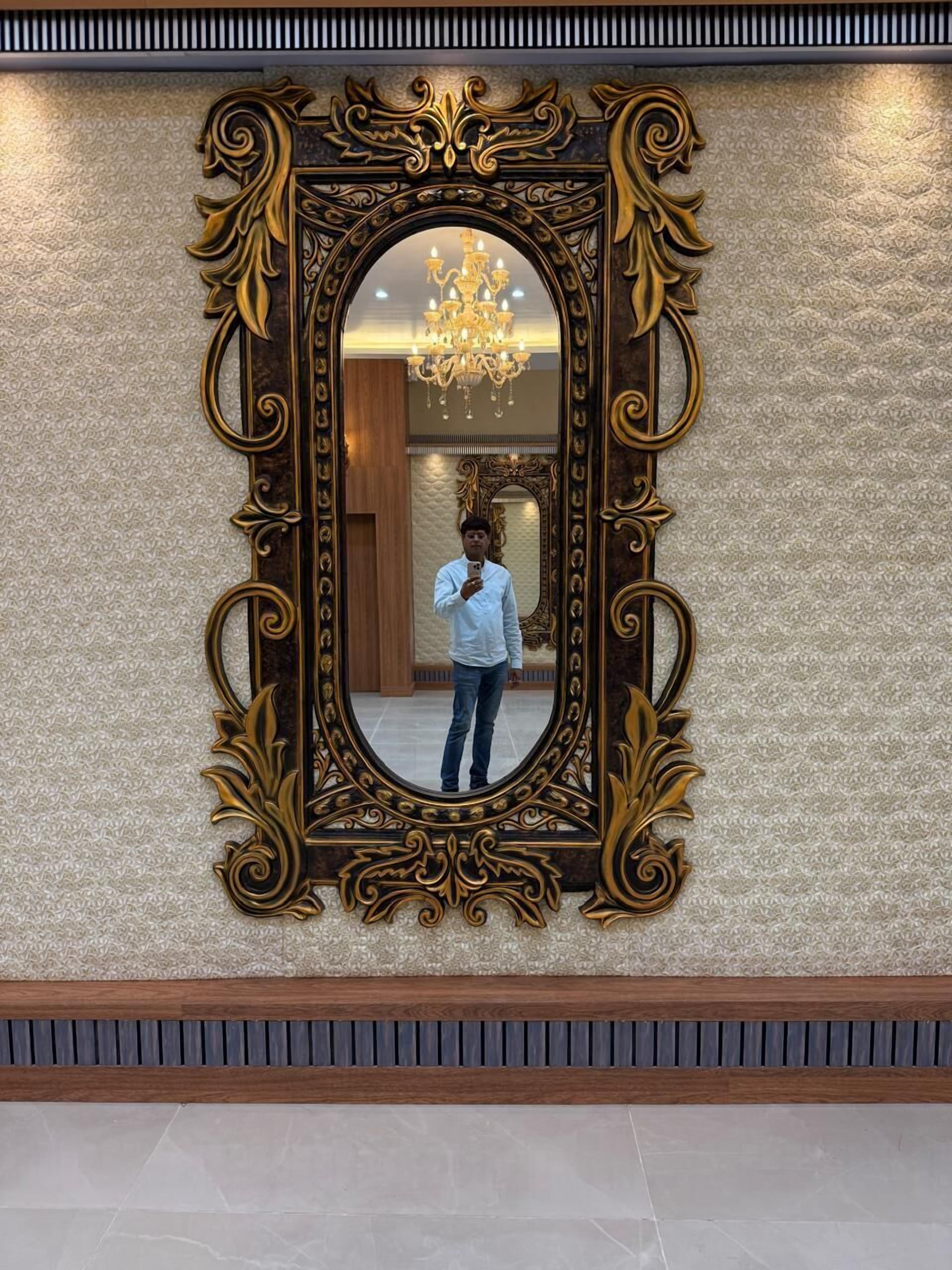 Un grand miroir décoratif, doté d’un cadre doré, est fixé sur un mur à texture.