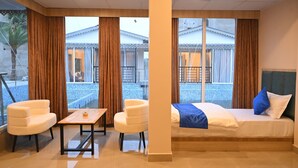 Habitación de hotel con cama, dos sillas, una mesita y ventanas amplias que ofrecen vistas al exterior.