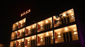 Un hotel de varios pisos con balcones, señalización iluminada e iluminación interior cálida.