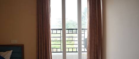 A hotel room with a bed, a window with curtains, and a view of a balcony with a railing.