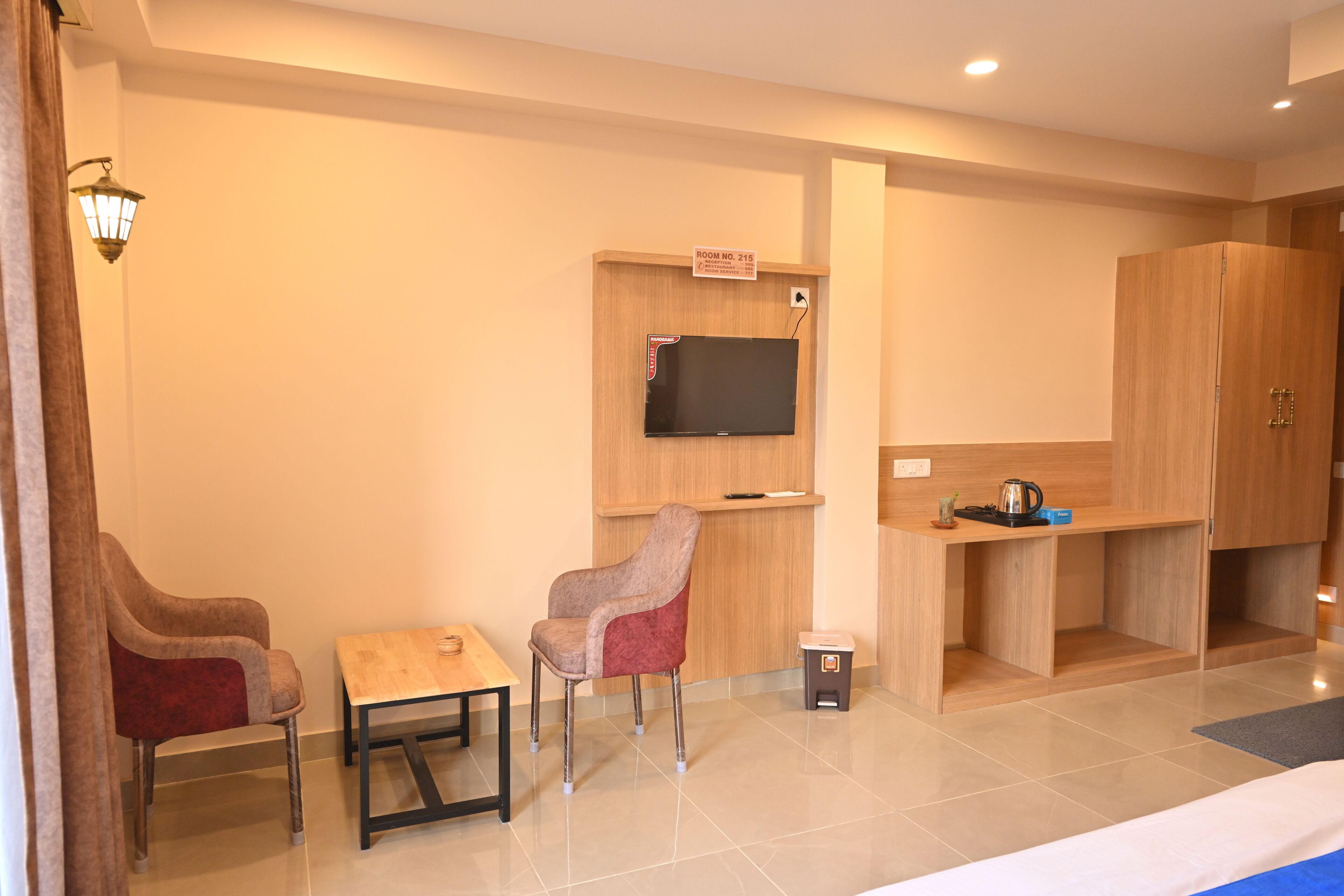 Habitación de hotel con un escritorio de madera, dos sillas, un televisor y un armario.