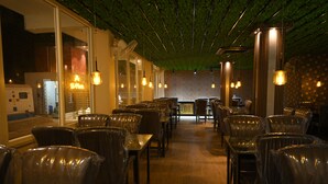 Un restaurante con filas de mesas y sillas, una pared de ladrillo y lámparas colgantes.