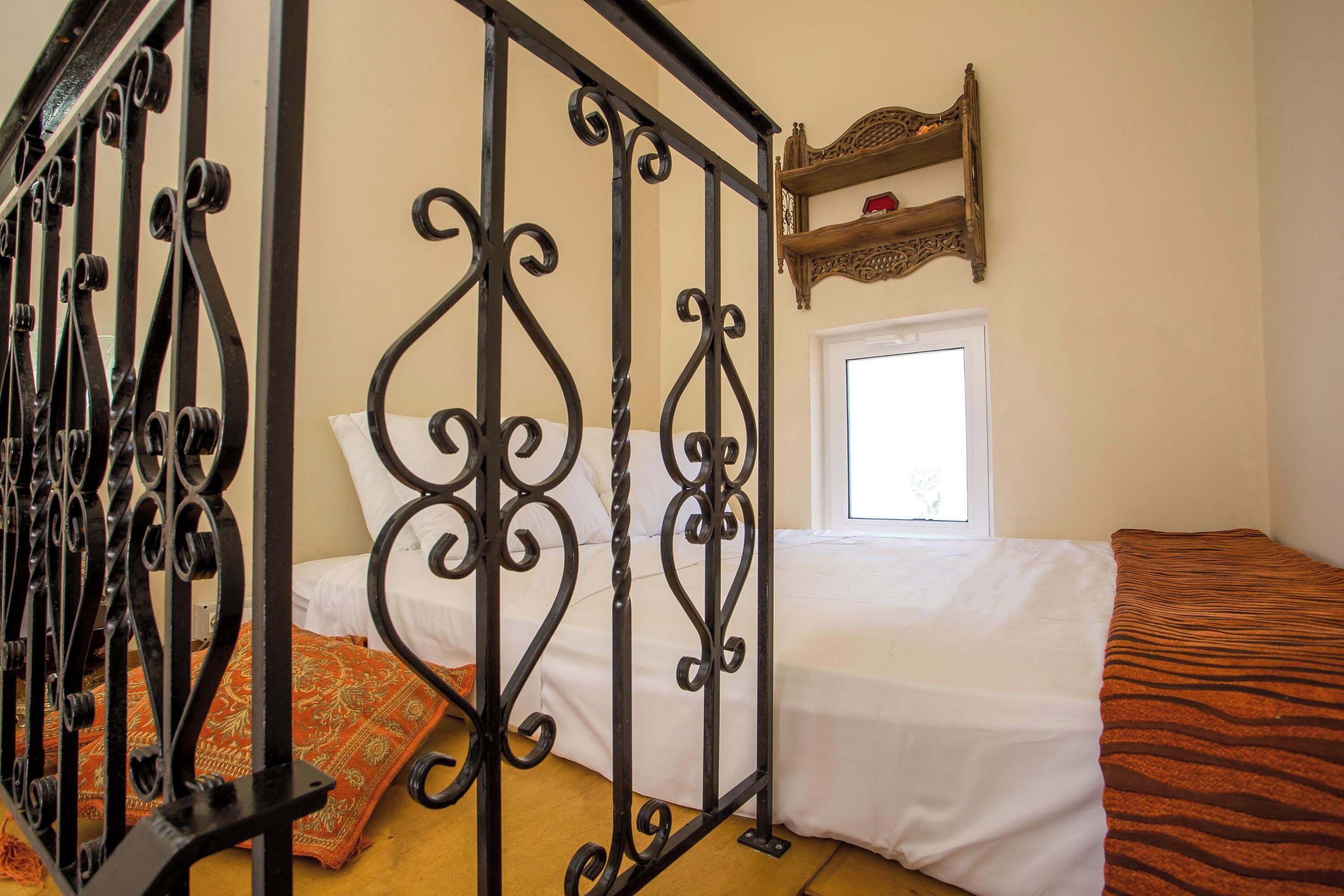 Ein Schlafzimmer mit einem Bett, einem Fenster, einem dekorativen Metallgitter und einem Regal mit einem roten Gegenstand.