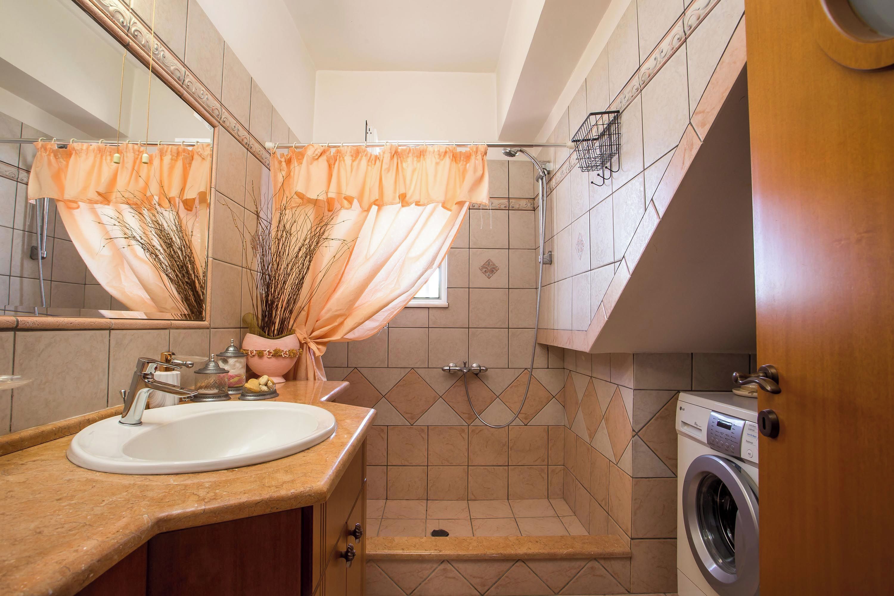Een badkamer met wastafel, spiegel, douche en wasmachine.