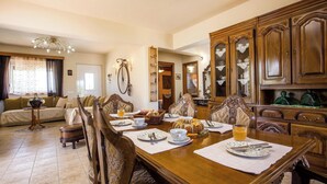 A dining room with a wooden table set for four, surrounded by ornate chairs, a chandelier, and a view into the kitchen. - Laylande House with Private Pool (Theologos)