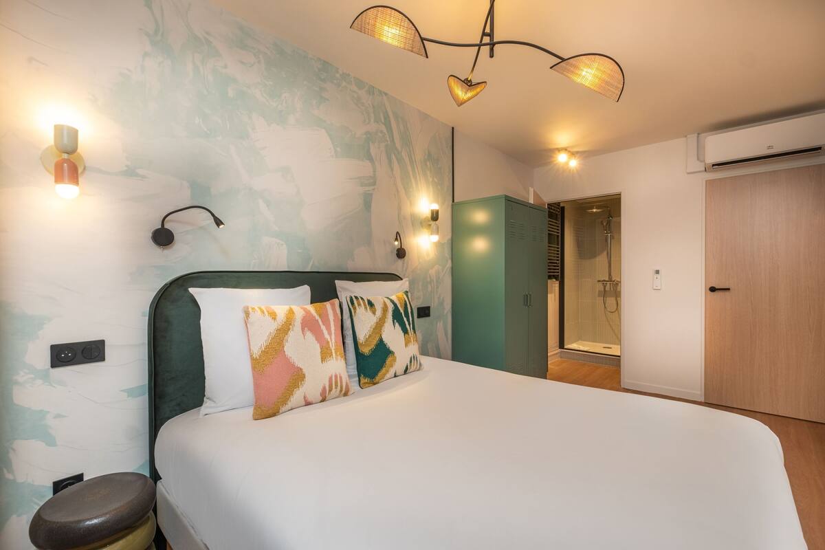 A hotel room with a bed, a wall-mounted light fixture, a shower area, and a wardrobe.