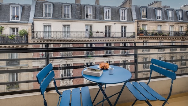 A balcony with two blue chairs and a small round table, a book, and a croissant. - Montmartre Paris Suite (Paris)
