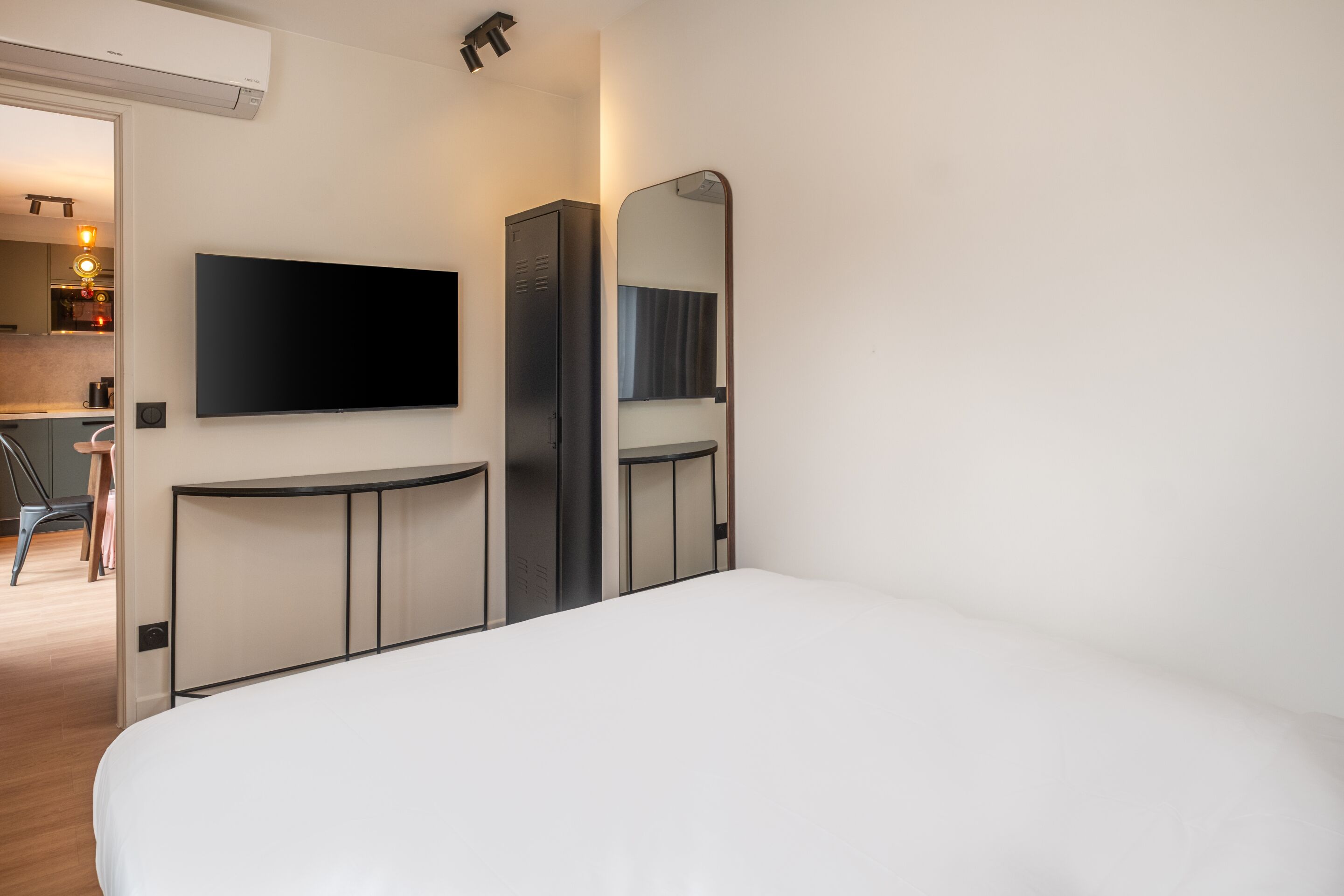 A modern hotel room with a large bed, a flat-screen TV mounted on the wall, a wardrobe, and a mirror.