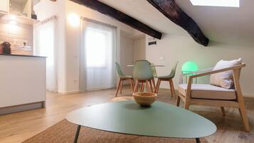 Una stanza accogliente con un tavolo rotondo, una sedia verde, una sedia di legno e un letto con un cuscino.