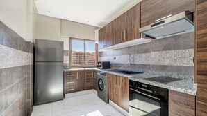 A modern kitchen with stainless steel appliances, wooden cabinets, and a large window offering a city view.