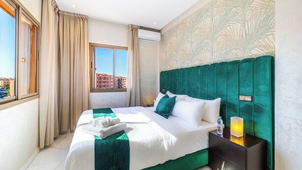 A hotel room with a large bed, a nightstand, a window with curtains, and a view of buildings outside.