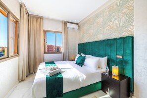 A hotel room with a large bed, a nightstand, a window with curtains, and a view of buildings outside.