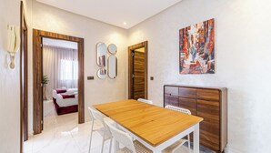 A modern hotel room with a wooden dining table, white chairs, a large mirror, and a painting on the wall.
