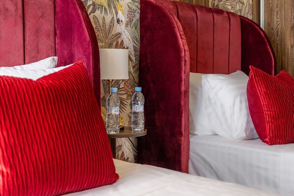 A bed with red pillows, a bedside table with water bottles, and a floral-patterned wall.