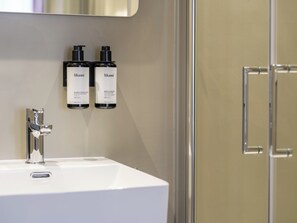 A bathroom with a white sink, two bottles of body lotion, and a mirror. - Lits de lo (Ghent)