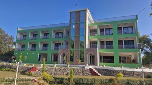Un edificio de varios pisos con balcones, una torre central de piedra y fachada verde.