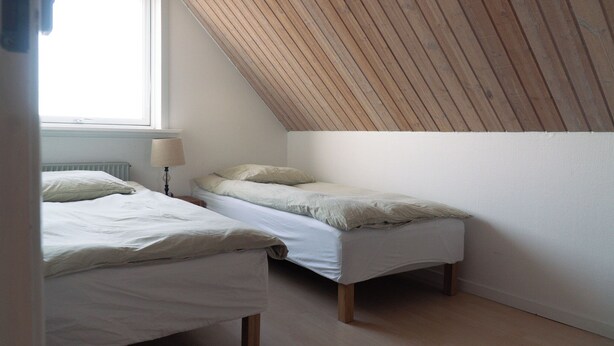 A small, simple room with two beds, a radiator, and a sloped ceiling. - Noah's Ark Homestay (Thisted)