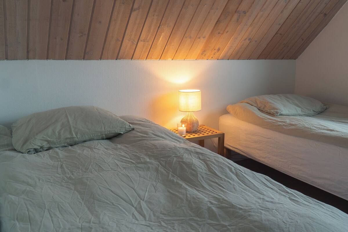 A bedroom with two beds, a nightstand with a lamp, and a wooden ceiling.