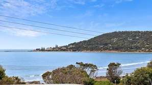 A coastal landscape with a clear sky, a body of water, and a hilly terrain in the background. - Beachfront 63 (Lorne)