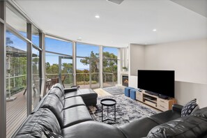 A modern living room with a large TV, leather sofa, and a balcony with a view.