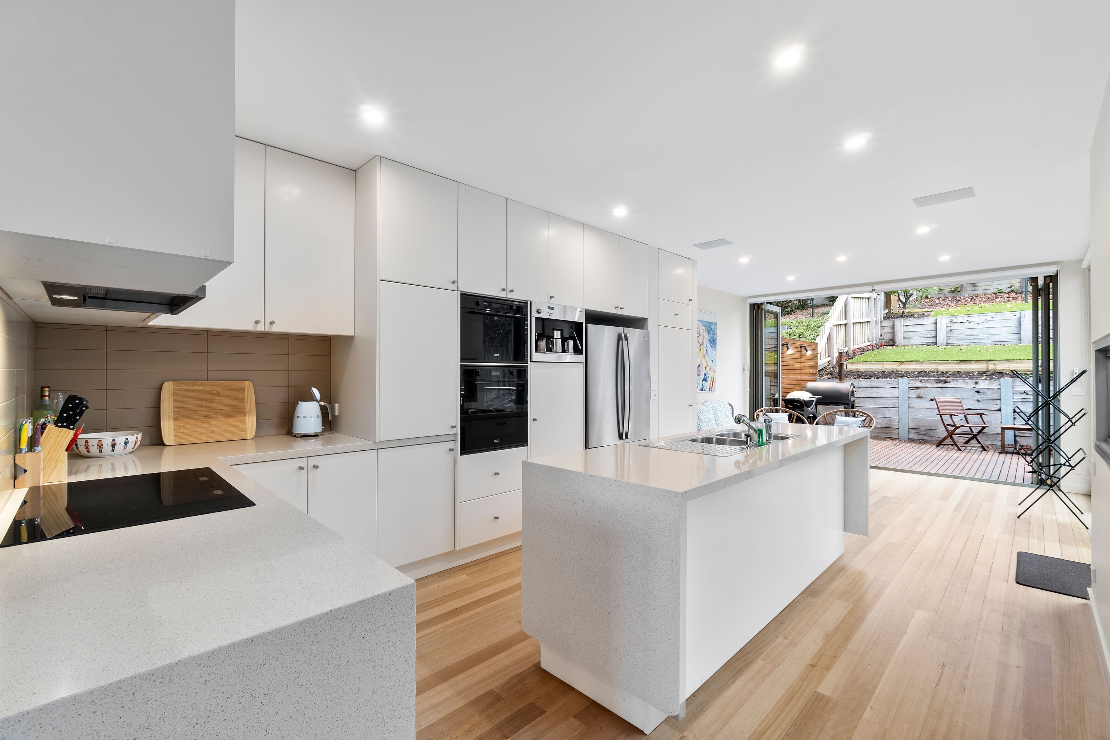 Een moderne keuken met een centraal eiland, inbouwapparatuur en uitzicht op een terras.