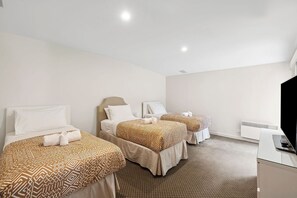 Een hotelkamer met drie bedden, een flatscreen televisie en een bureau.
