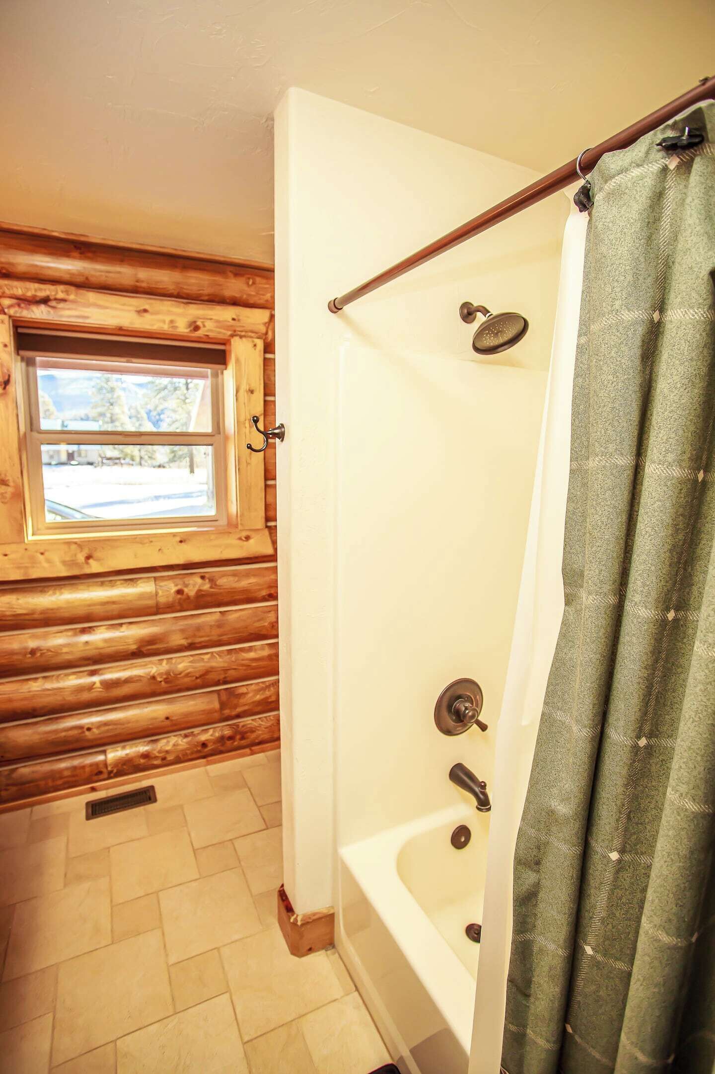 Ein Badezimmer einer Holzhütte mit Fenster, einer Badewanne und einer Duschvorhang.