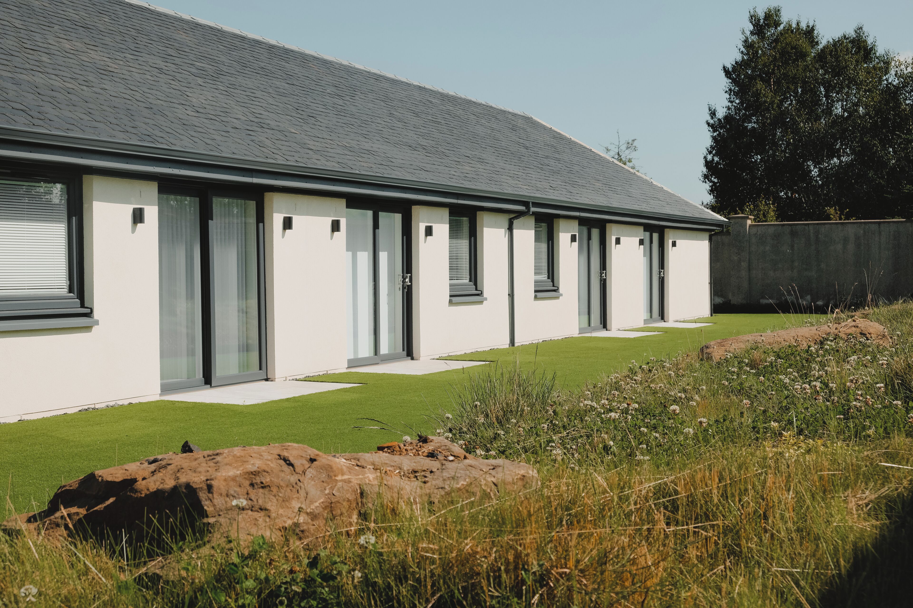 A modern house with a long, flat roof, large windows, and a well-maintained lawn.