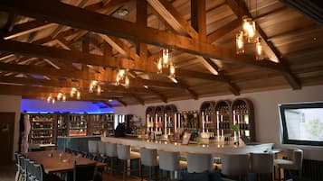 A bar area with wooden beams, hanging lights, and a bar counter with stools.