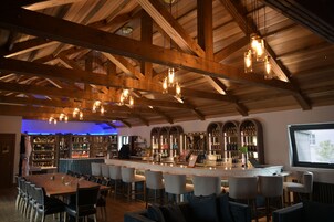 A bar area with wooden beams, hanging lights, and a bar counter with stools.