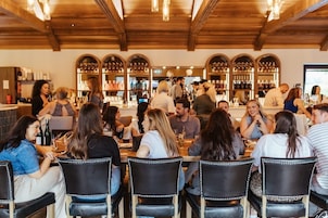 En restaurant med træbjælker i loftet, borde med stole og et barområde med flasker på hylder.